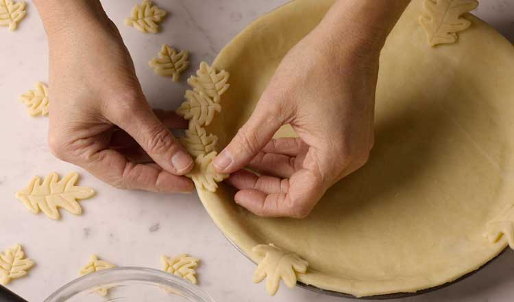 Adding leaves cut from crust dough to the edges of a pie crust for decoration.