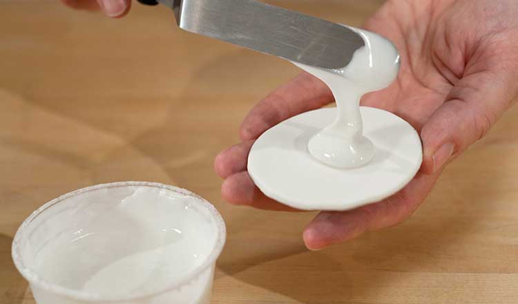 Pouring white royal icing onto cookie.