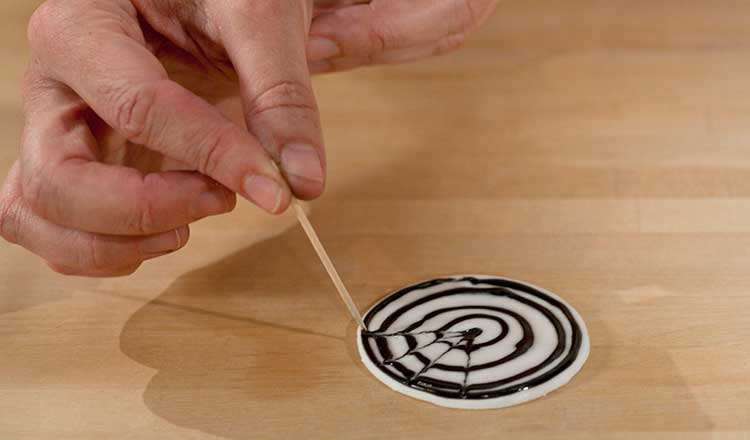 Using a toothpick to spread the black icing into a spiderweb pattern.