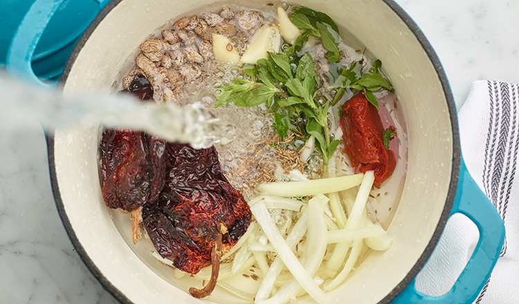 Creamy pinto bean ingredients in a pot with water being added