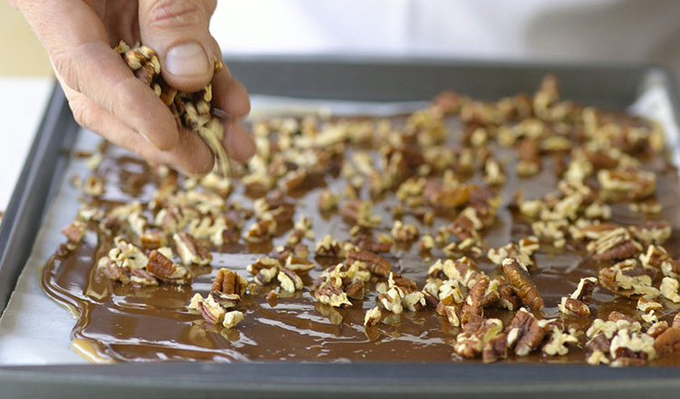 chocolate-coated toffee being sprinkled with pecans