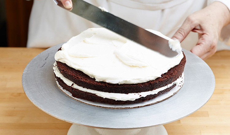 Spreading buttercream over layers of chocolate cake