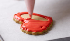 Decorating heart-shaped cookie with red royal icing.
