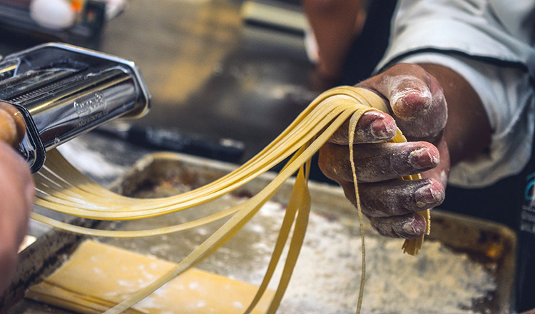 Rolling homemade pasta through a mechanical roller.