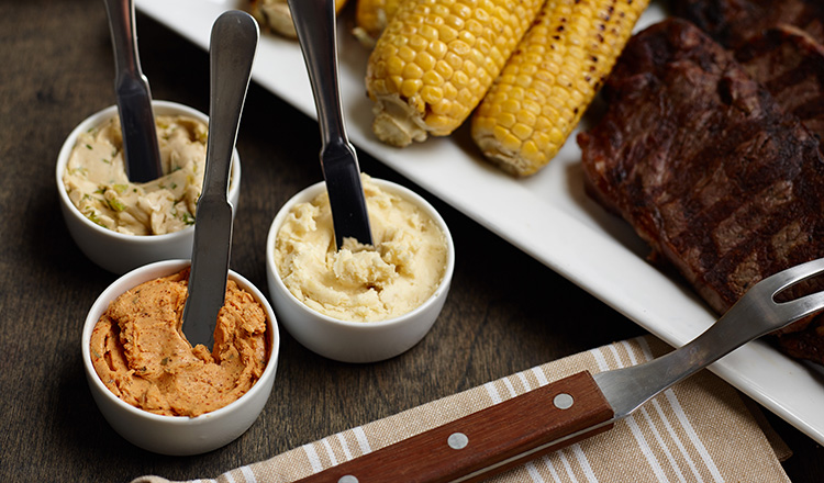 A trio of compound butters with grilled meats and vegetables.