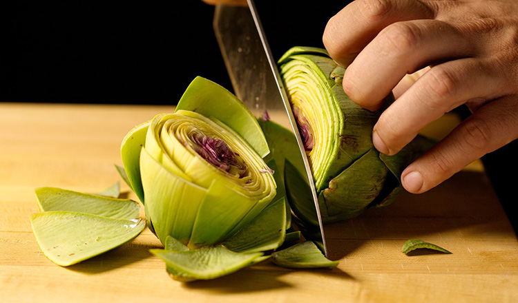 Cutting an artichoke on a wooden cutting board.