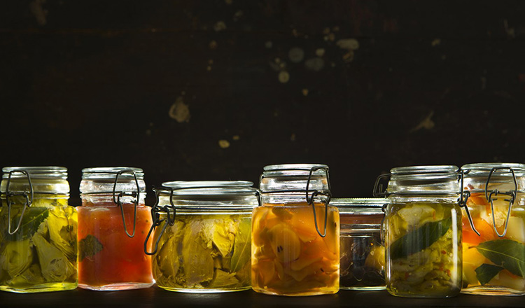 A variety of preserved food in glass jar. From left to right: artichokes, tomatoes, tuna, pears, olives, eggplants, mixed vegetables.