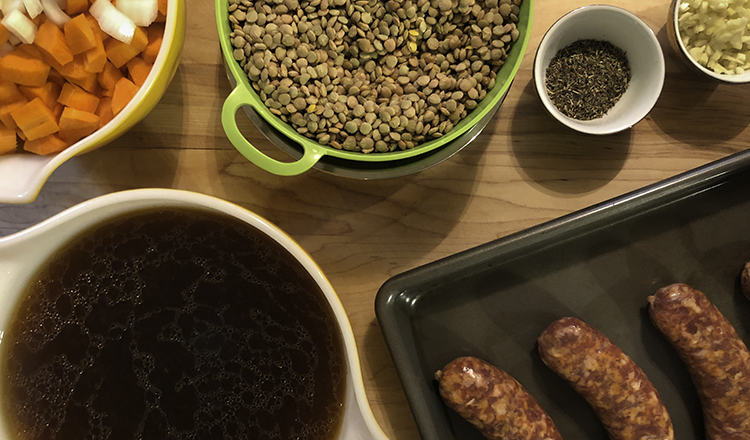 Ingredients for lentil soup: onion, carrot, lentils, thyme, garlic, sausage, and broth