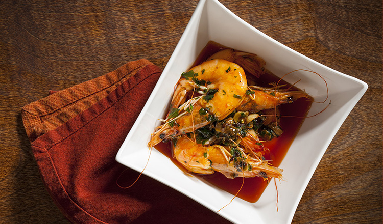 Shrimp in a garlic sauce served in a white square bowl.