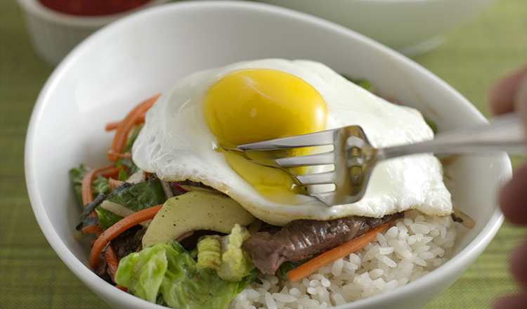 Bibimbap, mixed vegetables and meat over rice with hot sauce.