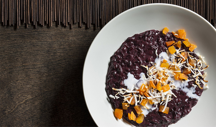 Purple rice pudding with dried mangos and toasted shredded coconut in a white round bowl.