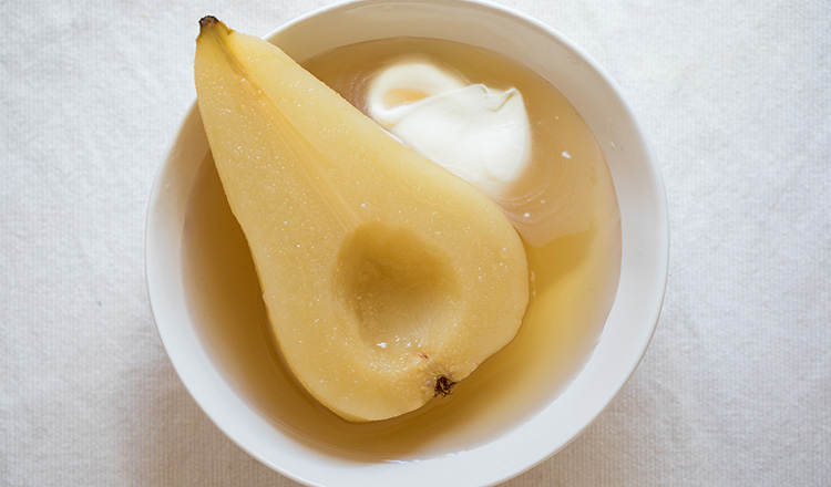 Cardamom poached pear with creme fraiche in a round white bowl