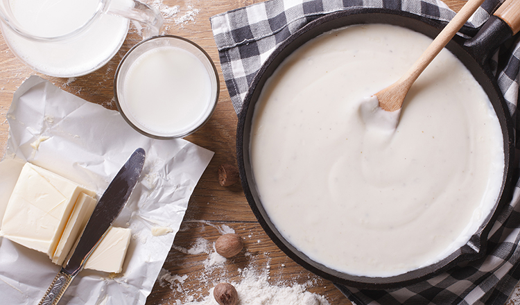Preparation of bechamel sauce in a pan and ingredients on the table.