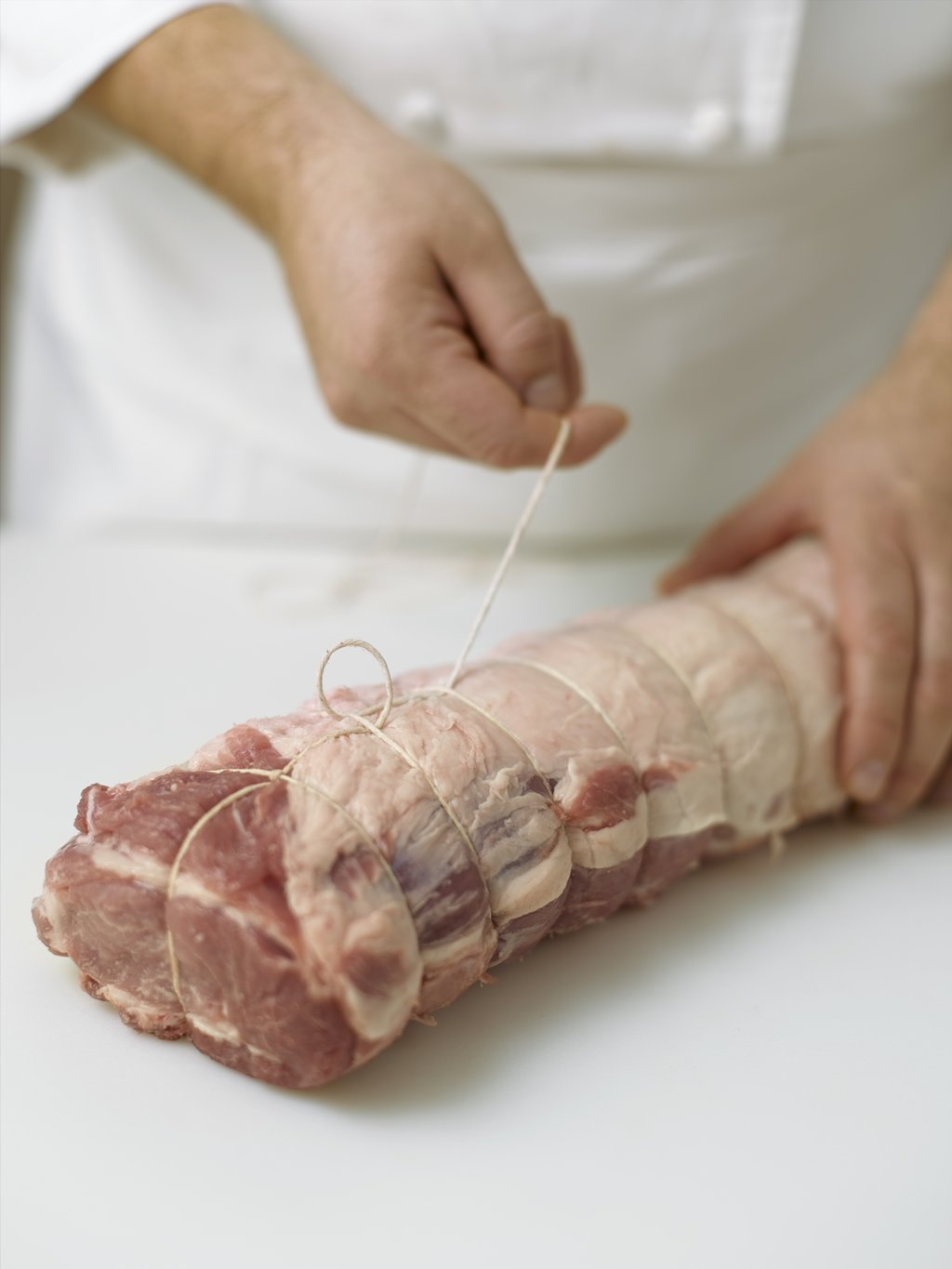 Step six: Turn the piece of meat over. Pass the loose end of the string through the loop, then pass it back around and underneath the loop. Pull the string tight and continue down the length of the meat.