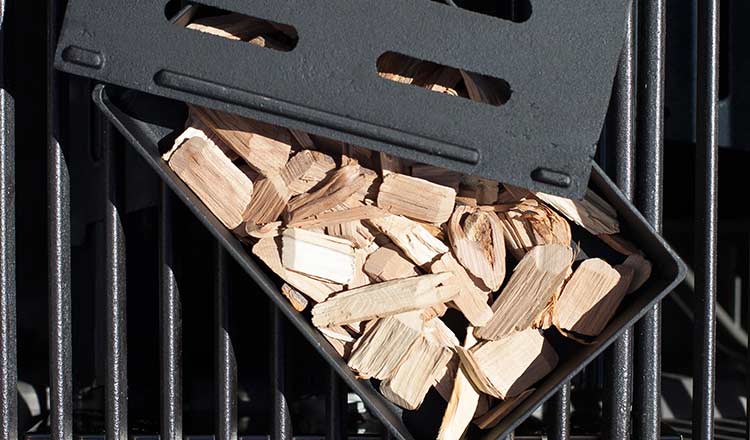 Wood chips in a smoker box, sitting on grill grates