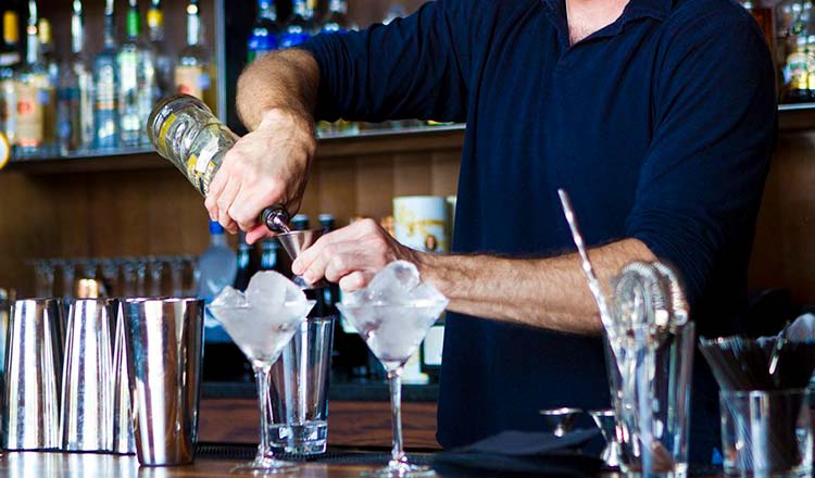 Man in blue shirt mixing cocktails at a bar