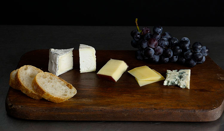 Cheeses on a board with grapes and bread