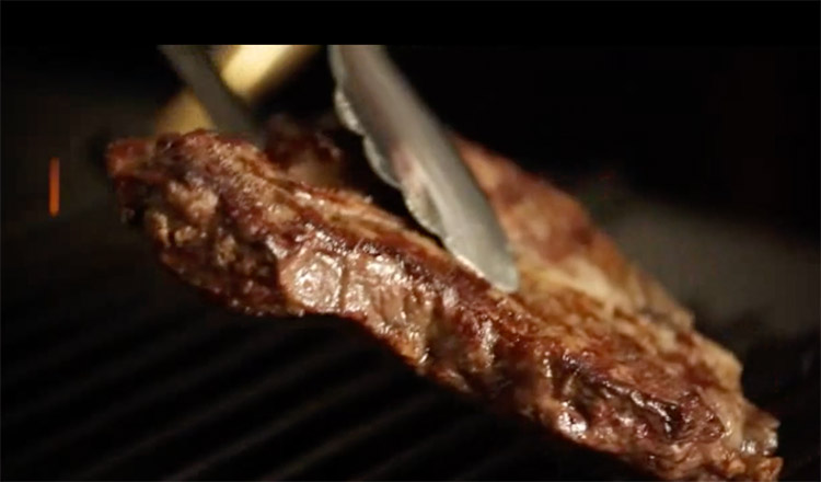 Tongs flipping a cooked steak on a grill