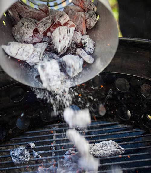 Hot coals being poured into a charcoal grill