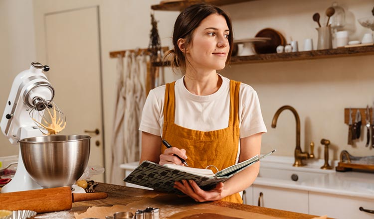 Woman in kitchen holding notebook and pen