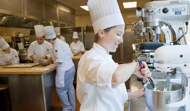 Student in chef's whites using a stand mixer