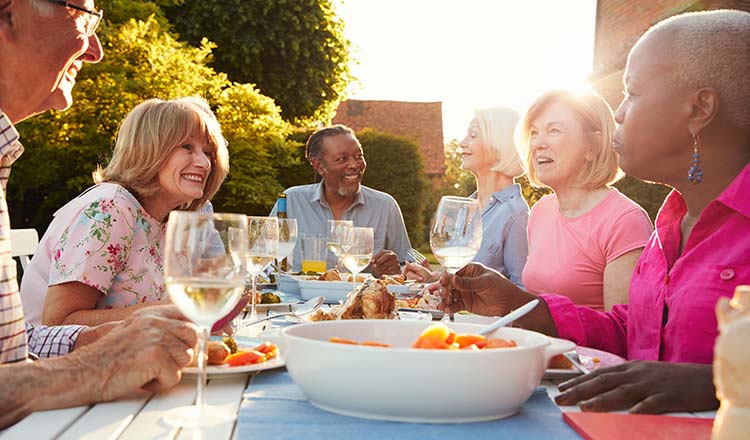 Adults at a table outdoors drinking wine and eating food