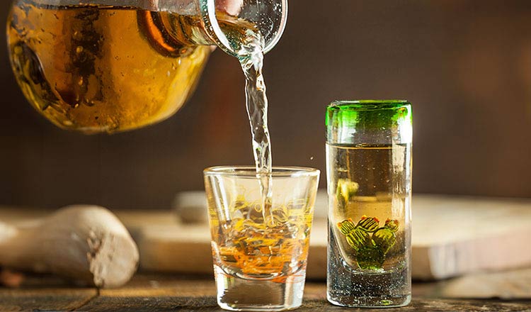 Image of someone pouring tequilla into a shot glass with another full shot glass.