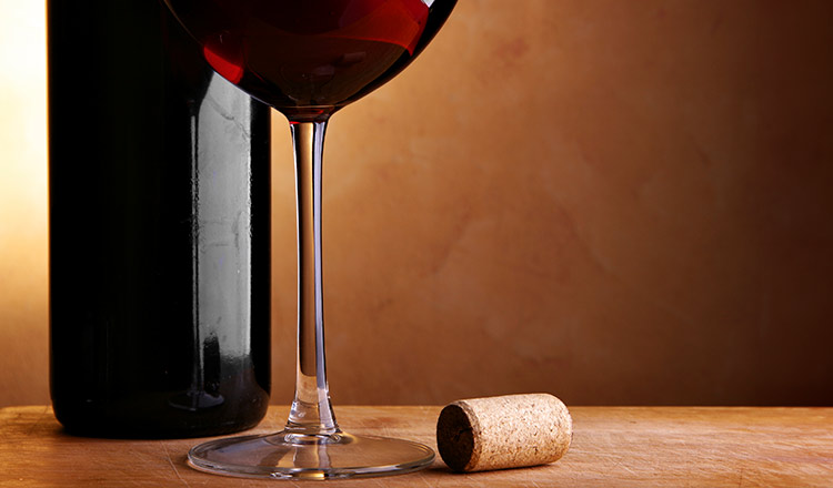 Image of a red wine bottle, wine glass, and cork on a table.