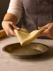 Placing pie dough in a metal pie pan