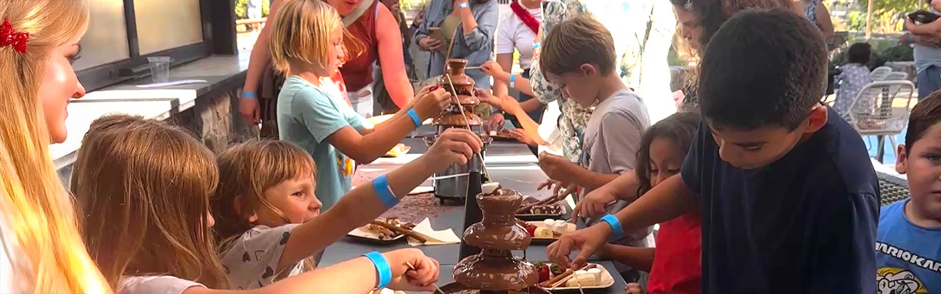 Children at CIA at Copia’s Flavors of Film Series dip treats in a chocolate fountain, smiling.