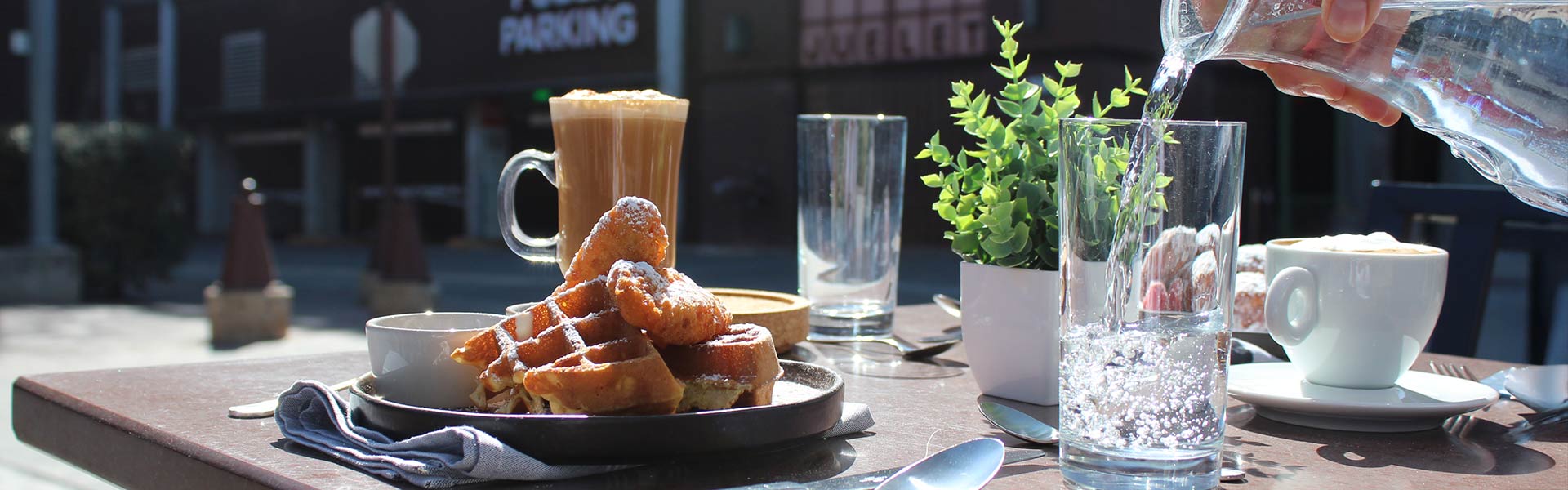 CIA Bakery Café outdoor table with waffles, pastries, coffee drinks, and water being poured into a glass.